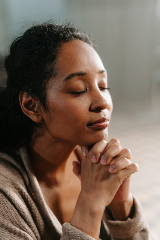 A women clasping her hands by her chin with eyes closed praying with a blurred background.