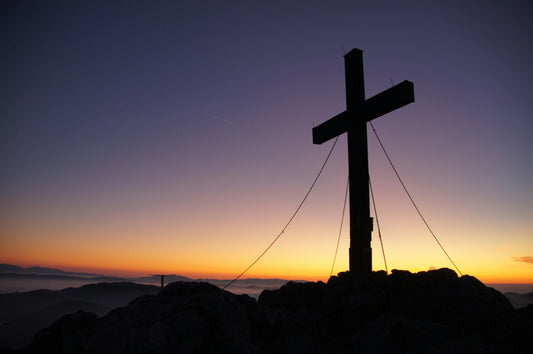 The cross of Jesus Christ held up with cords against a sunset, purple and yellow sky. Moody sky background.