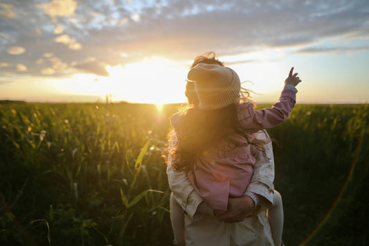 Sunny background in a field with green plants. A woman holding a child with a pink coat. 