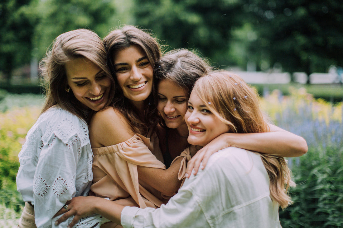 Four women hugging and expressing gratitude and thanks for each other and nature with plants blurred in the background.