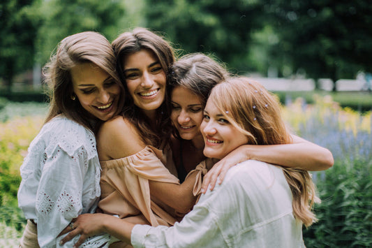 Four women hugging and expressing gratitude and thanks for each other and nature with plants blurred in the background.
